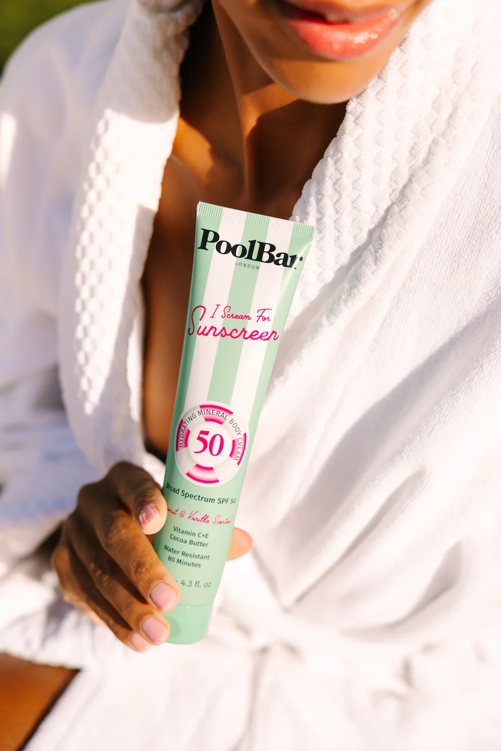 woman in dressing gown holding poolbar spf 50 mineral sunscreen