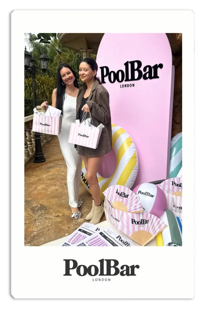 2 woman smiling whilst holding poolbar gift bags from clean magazine event polaroid