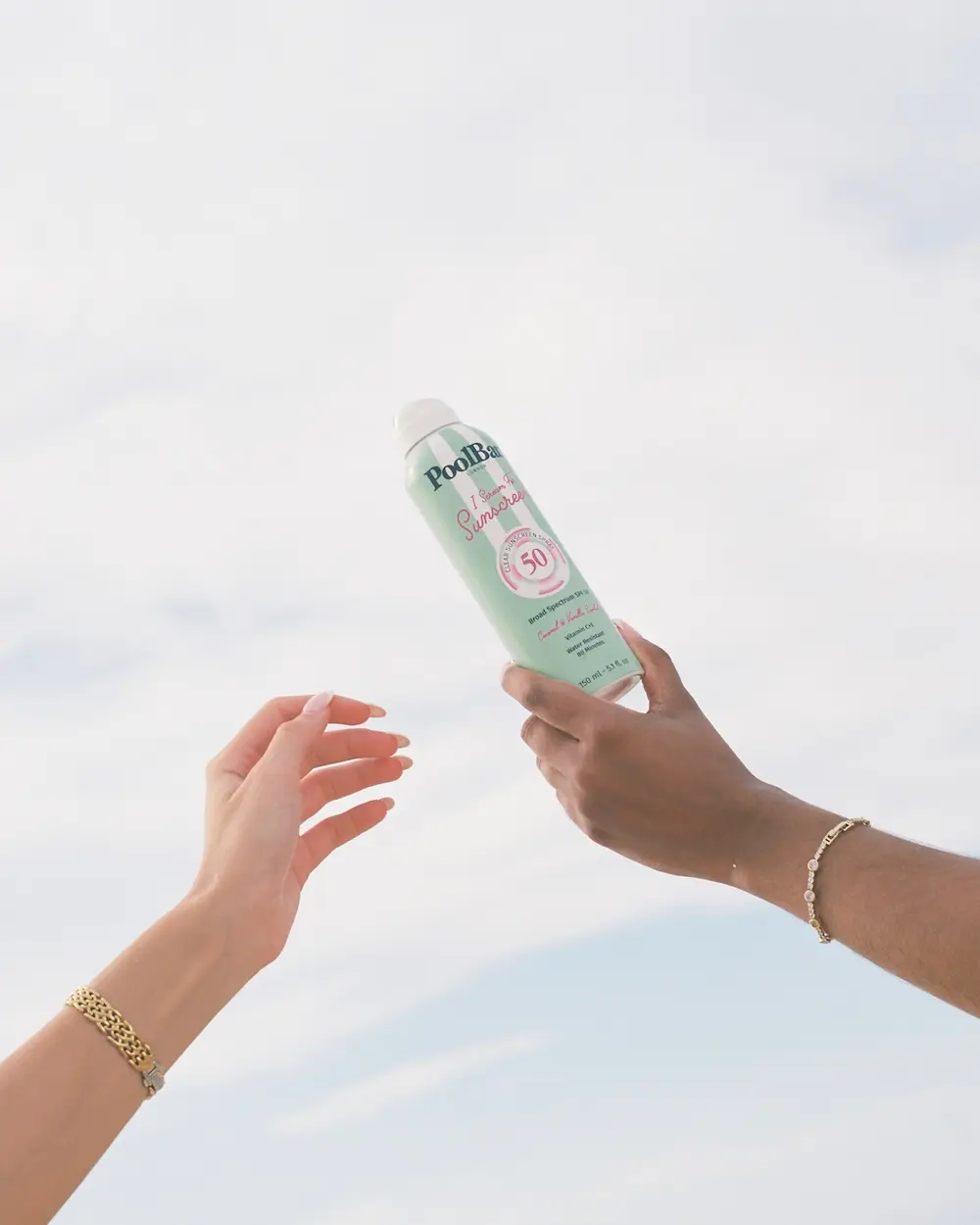 Two hands in the air with one holding a green SPF Spray can