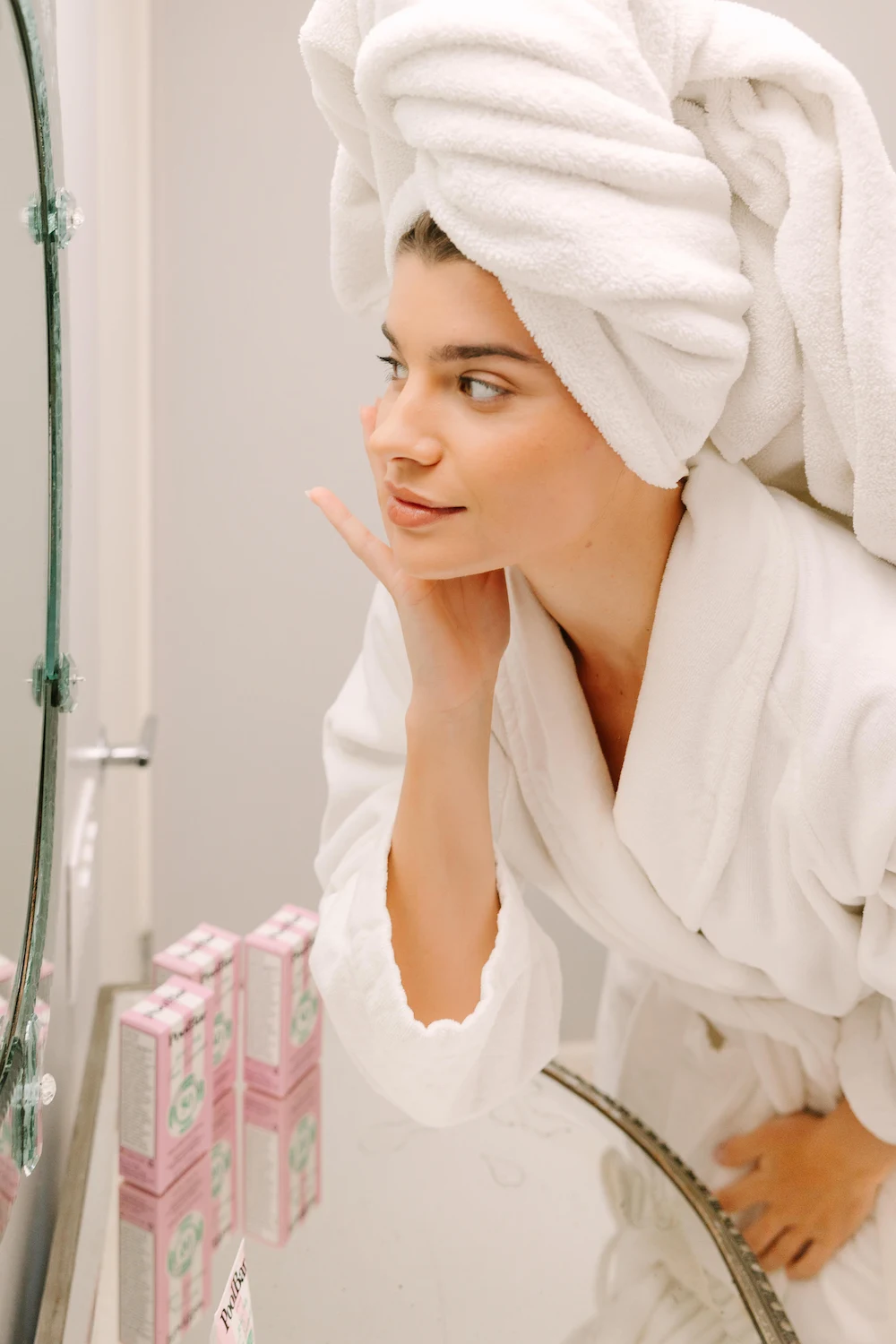 woman in bath robe and hair towel applying face sunscreen in the bathroom mirror